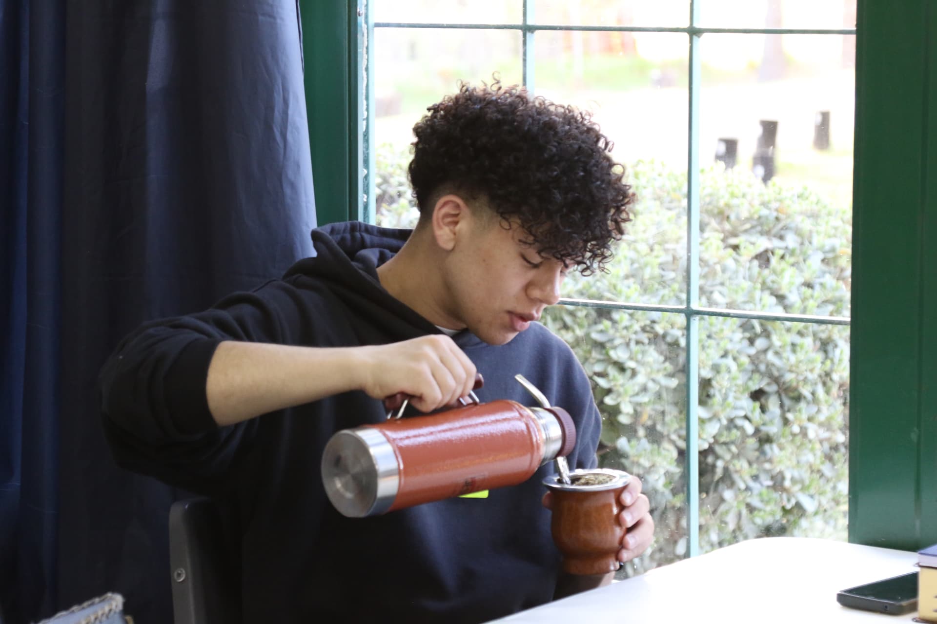 Estudiante cebando mate junto a la ventana
